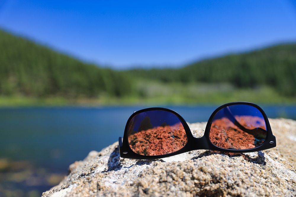 Polarized sunglasses on top of a rock by a lake